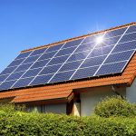 Solar panel on a red roof reflecting the sun and the cloudless blue sky